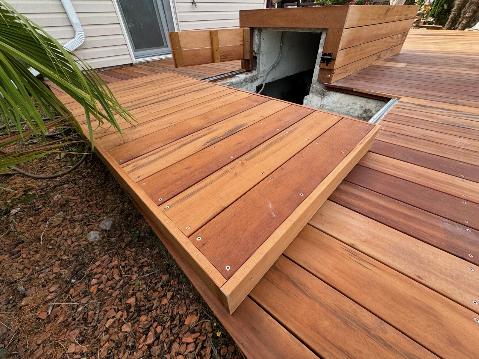 Design raffiné et solution astucieuse : La trappe coulissante dissimule parfaitement l'accès au local technique, tout en préservant l'harmonie de cette terrasse en Tiger Wood à Saint-Sulpice.
